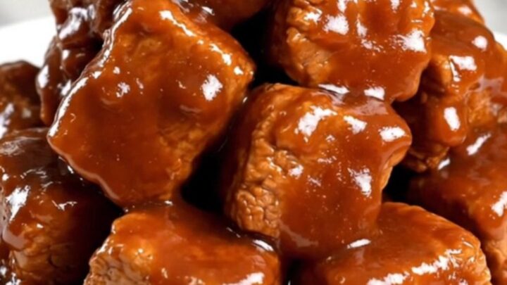 A close-up of tender, saucy pork burnt ends in a slow cooker, featuring a rich, dark glaze and visible spice rub.