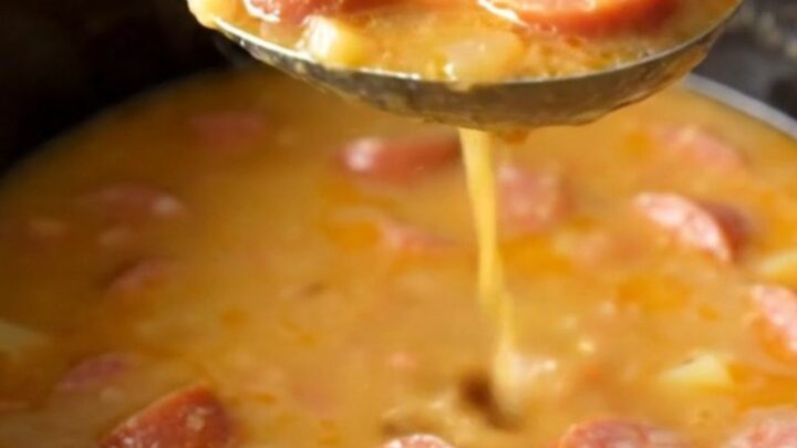 A close-up of a bowl filled with creamy sausage and potato soup with visible sausage coins and sun-dried tomatoes.