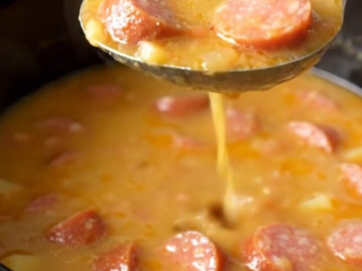 A close-up of a bowl filled with creamy sausage and potato soup with visible sausage coins and sun-dried tomatoes.