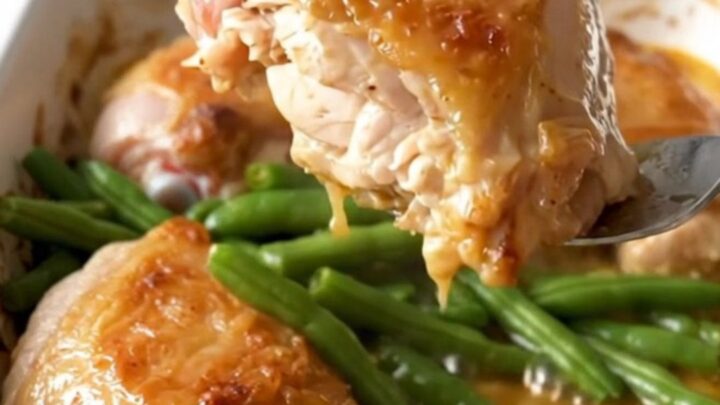 A ceramic baking dish filled with golden baked chicken thighs and bright green beans in a lemon butter sauce.