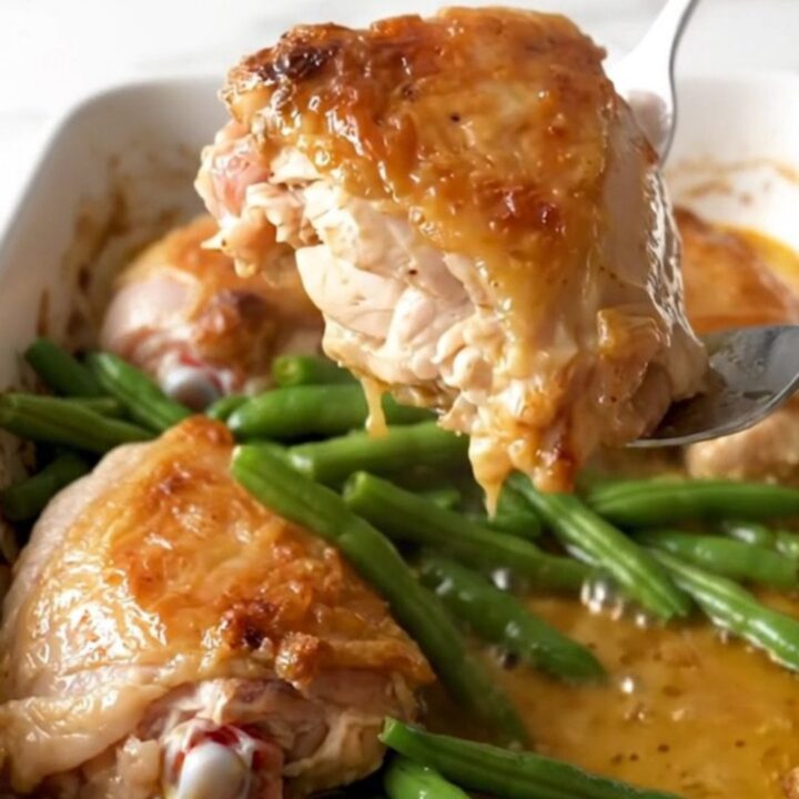 A ceramic baking dish filled with golden baked chicken thighs and bright green beans in a lemon butter sauce.