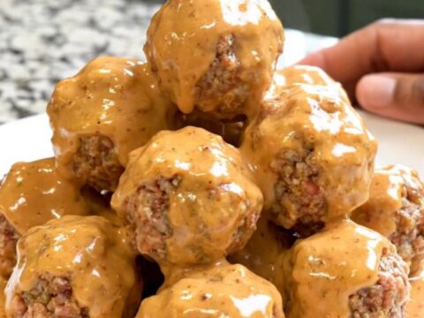 A close-up of glossy Bang Bang Meatballs in a black slow cooker bowl on a granite countertop.