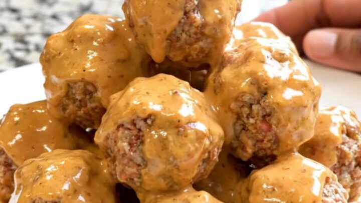 A close-up of glossy Bang Bang Meatballs in a black slow cooker bowl on a granite countertop.