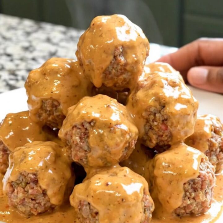 A close-up of glossy Bang Bang Meatballs in a black slow cooker bowl on a granite countertop.