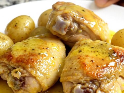 A top-down view of six raw boneless chicken thighs and halved gold potatoes in a black slow cooker insert.