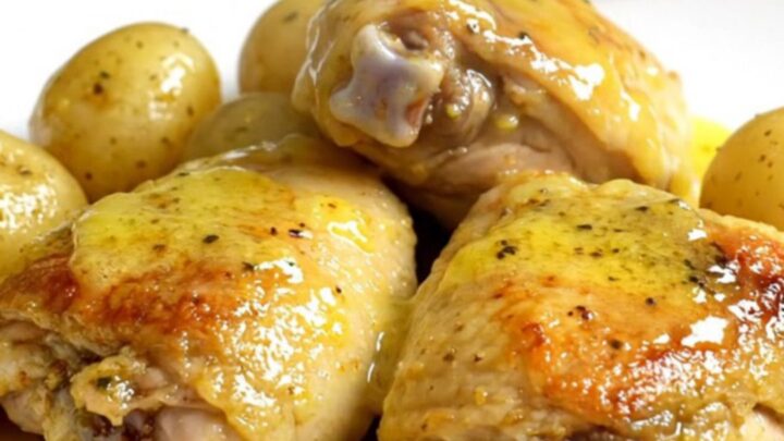 A top-down view of six raw boneless chicken thighs and halved gold potatoes in a black slow cooker insert.