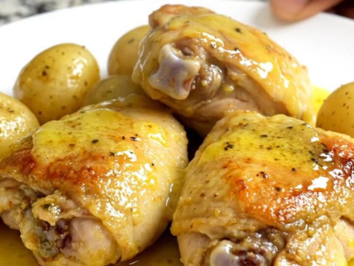 A top-down view of six raw boneless chicken thighs and halved gold potatoes in a black slow cooker insert.