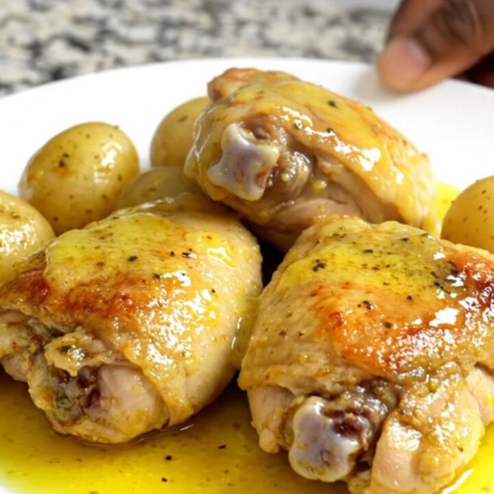 A top-down view of six raw boneless chicken thighs and halved gold potatoes in a black slow cooker insert.