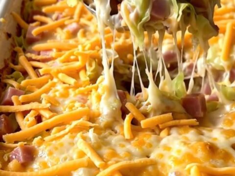 Top-down view of a ceramic baking dish filled with fresh cabbage, cubed ham, and creamy sauce topped with shredded cheddar.