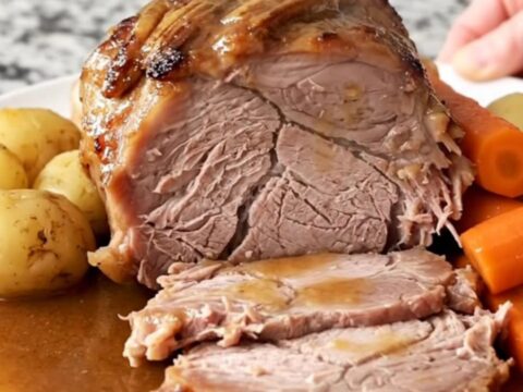 A slow cooker pork loin roast with potatoes and carrots served on a white plate with rich brown gravy.
