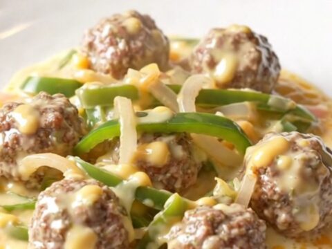 A close-up of tender beef meatballs covered in a creamy white provolone cheese sauce with colorful bell peppers.