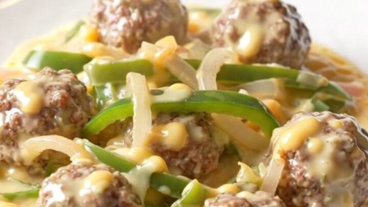 A close-up of tender beef meatballs covered in a creamy white provolone cheese sauce with colorful bell peppers.