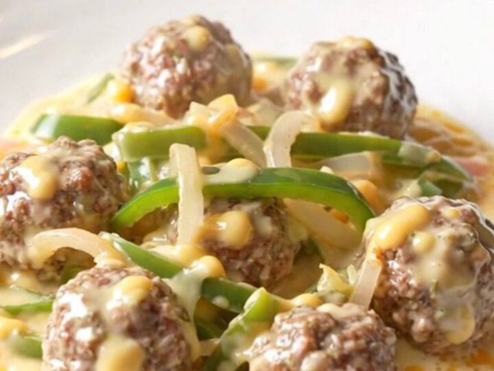 A close-up of tender beef meatballs covered in a creamy white provolone cheese sauce with colorful bell peppers.