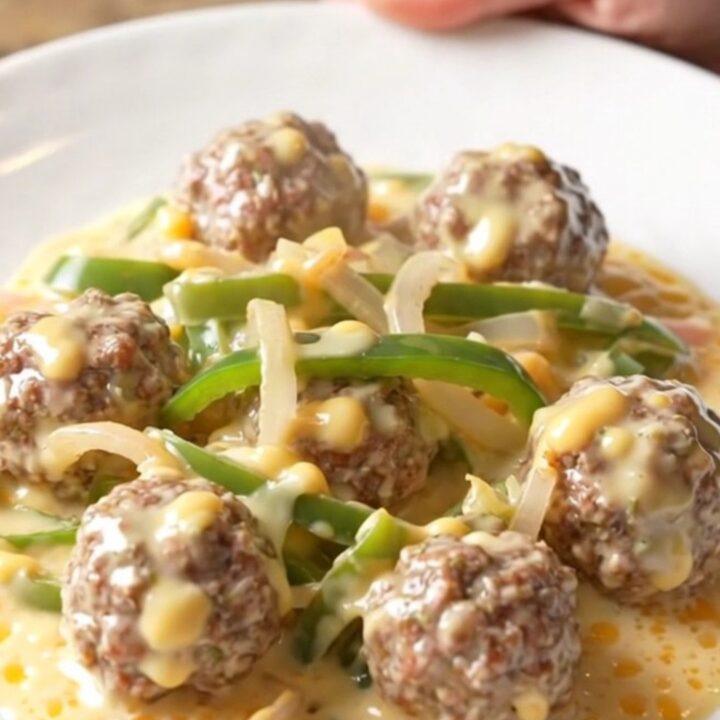 A close-up of tender beef meatballs covered in a creamy white provolone cheese sauce with colorful bell peppers.