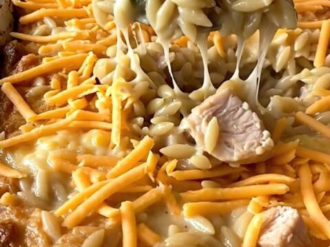 A top-down view of a rectangular ceramic baking dish filled with raw orzo, chicken, and broccoli on a granite countertop.