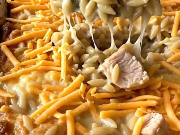 A top-down view of a rectangular ceramic baking dish filled with raw orzo, chicken, and broccoli on a granite countertop.