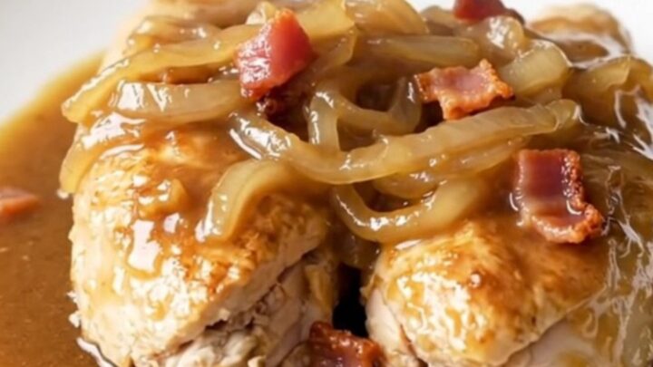 A close-up of tender chicken breasts covered in savory brown gravy, crispy bacon, and soft onions.