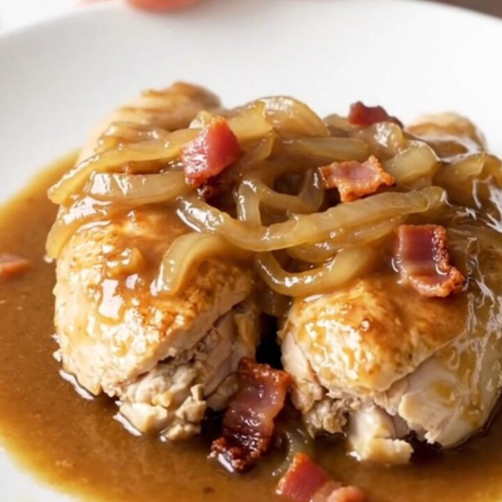 A close-up of tender chicken breasts covered in savory brown gravy, crispy bacon, and soft onions.