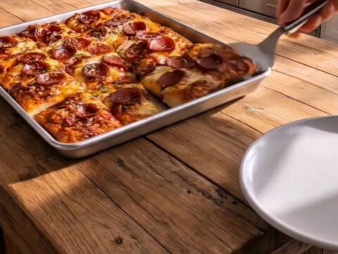 A golden, crispy sheet pan pizza with stretchy melted mozzarella and curled pepperoni slices.