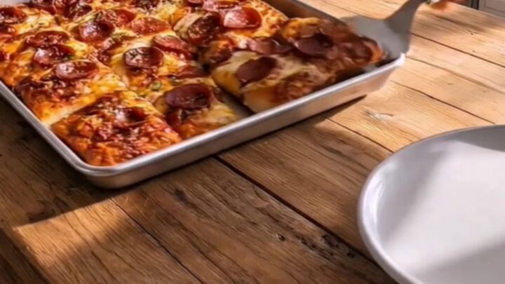 A golden, crispy sheet pan pizza with stretchy melted mozzarella and curled pepperoni slices.