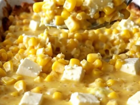A golden, bubbling honey butter corn casserole in a white ceramic dish on a speckled countertop.