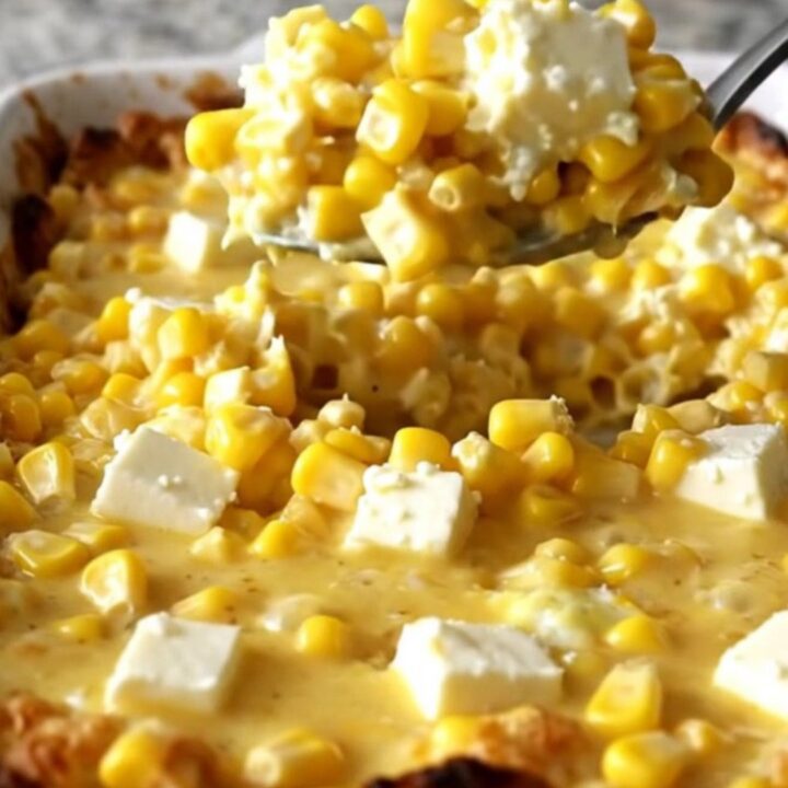 A golden, bubbling honey butter corn casserole in a white ceramic dish on a speckled countertop.