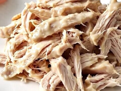 A white oval slow cooker filled with creamy shredded chicken topped with buttery cracker crumbs on a wooden counter.