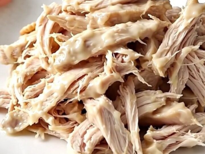 A white oval slow cooker filled with creamy shredded chicken topped with buttery cracker crumbs on a wooden counter.