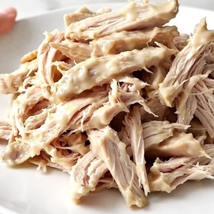 A white oval slow cooker filled with creamy shredded chicken topped with buttery cracker crumbs on a wooden counter.