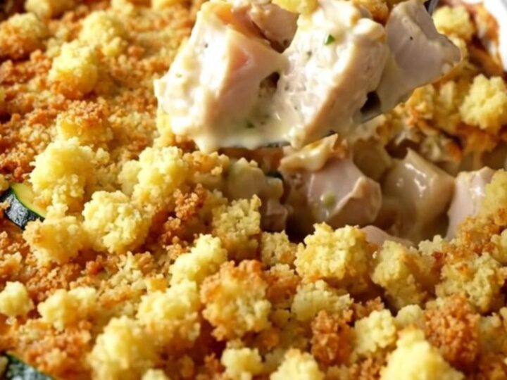 A top-down view of a golden, bubbling chicken and zucchini casserole in a white ceramic baking dish.