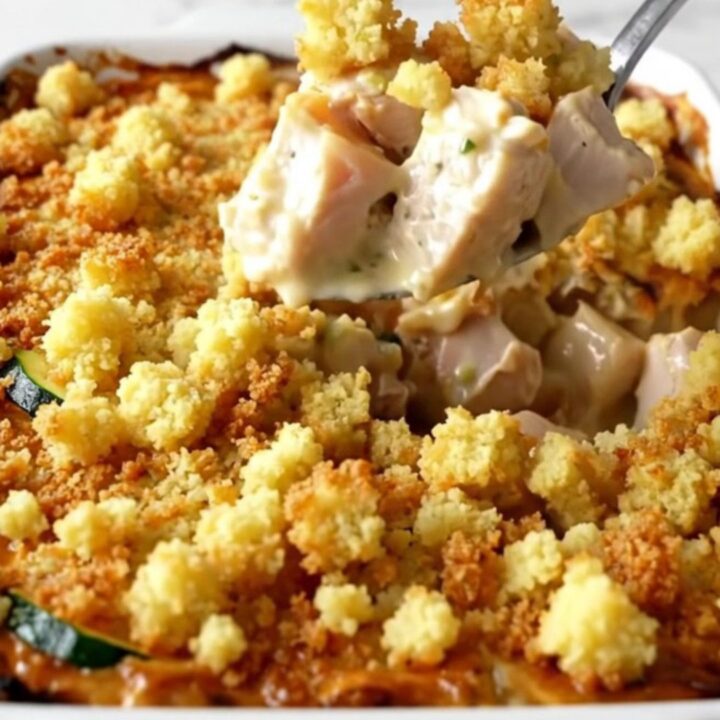 A top-down view of a golden, bubbling chicken and zucchini casserole in a white ceramic baking dish.