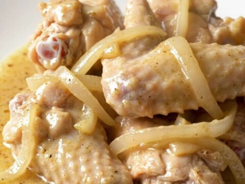 A slow cooker filled with chicken wings, sliced onions, and bell peppers in a creamy white gravy.