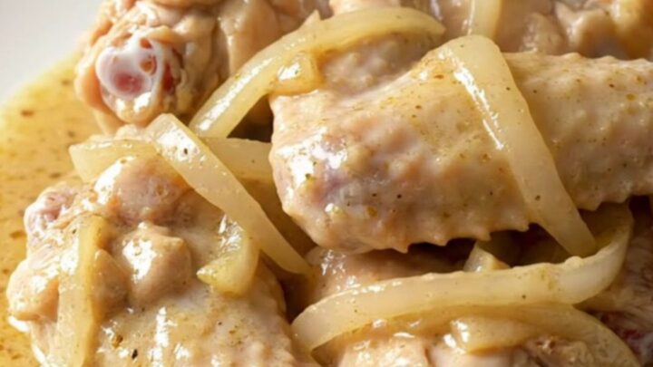 A slow cooker filled with chicken wings, sliced onions, and bell peppers in a creamy white gravy.