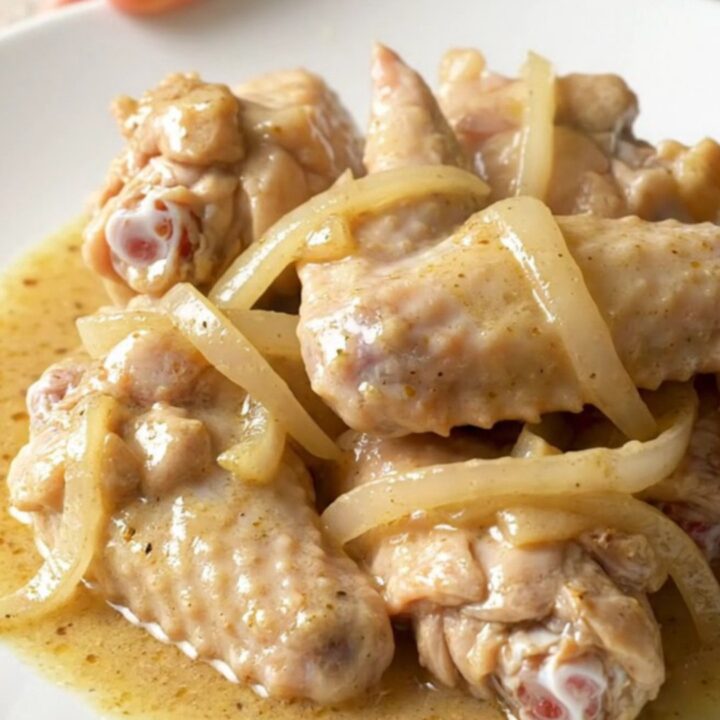 A slow cooker filled with chicken wings, sliced onions, and bell peppers in a creamy white gravy.