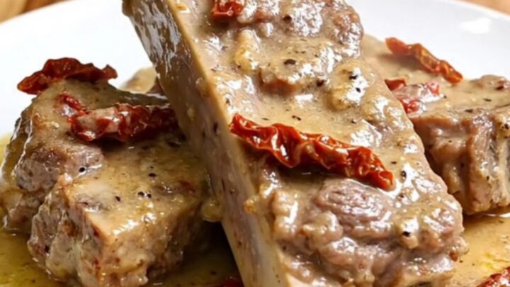 A close-up of tender, creamy pork ribs served on a white plate with sun-dried tomatoes and parmesan sauce.