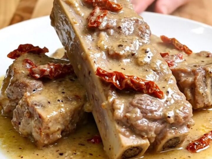 A close-up of tender, creamy pork ribs served on a white plate with sun-dried tomatoes and parmesan sauce.
