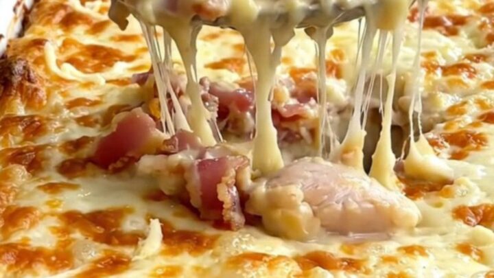 A large rectangular baking dish filled with creamy chicken and penne pasta, topped with melted mozzarella and crispy bacon.