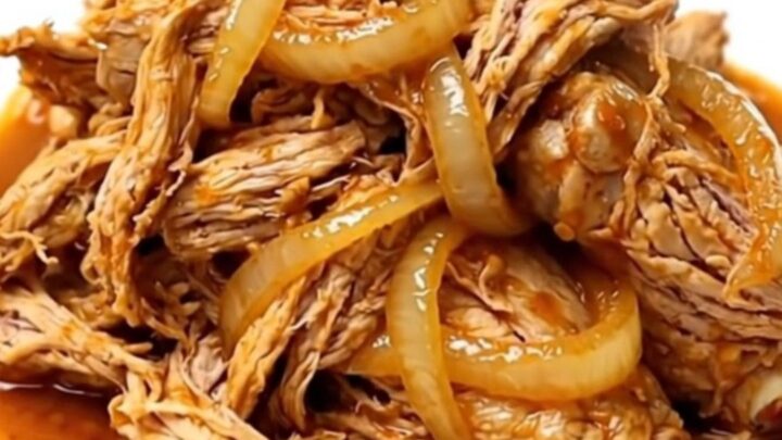 Slow cooker chicken barbacoa with shredded meat, onions, and chipotle sauce in a ceramic bowl.