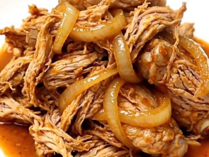 Slow cooker chicken barbacoa with shredded meat, onions, and chipotle sauce in a ceramic bowl.