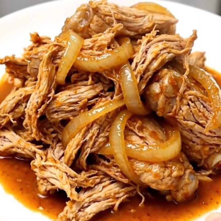 Slow cooker chicken barbacoa with shredded meat, onions, and chipotle sauce in a ceramic bowl.