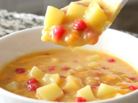 A bowl of creamy pimento cheese potato soup with visible potato cubes and red pimento bits.