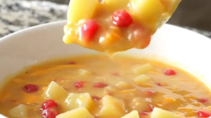 A bowl of creamy pimento cheese potato soup with visible potato cubes and red pimento bits.