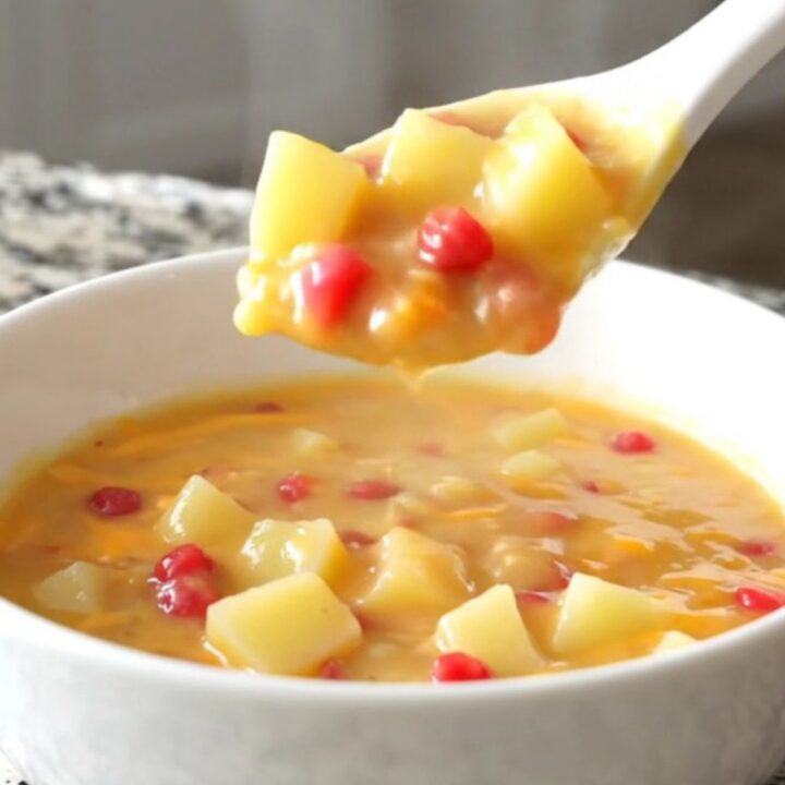 A bowl of creamy pimento cheese potato soup with visible potato cubes and red pimento bits.