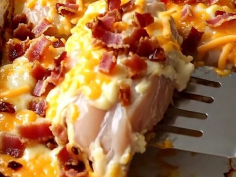 A golden, bubbling Creamy Bacon Cheddar Chicken Bake in a white ceramic dish on a rustic wood countertop.