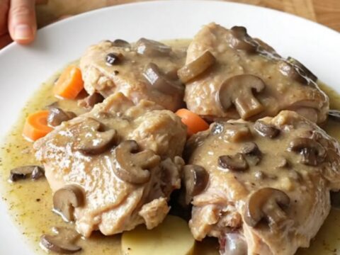 A top-down view of a slow cooker filled with chicken thighs, potato slices, and carrots in a creamy mushroom gravy.