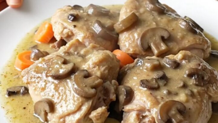 A top-down view of a slow cooker filled with chicken thighs, potato slices, and carrots in a creamy mushroom gravy.