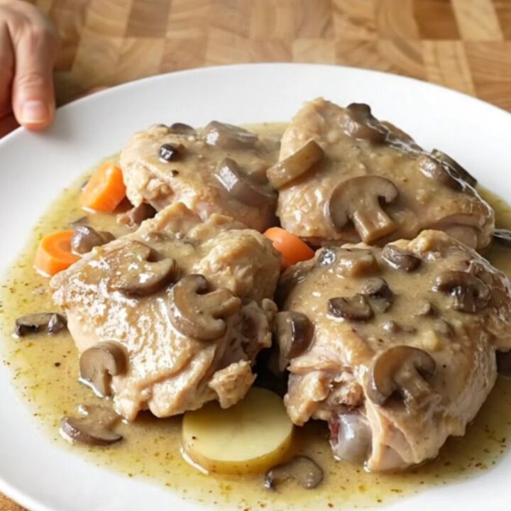 A top-down view of a slow cooker filled with chicken thighs, potato slices, and carrots in a creamy mushroom gravy.