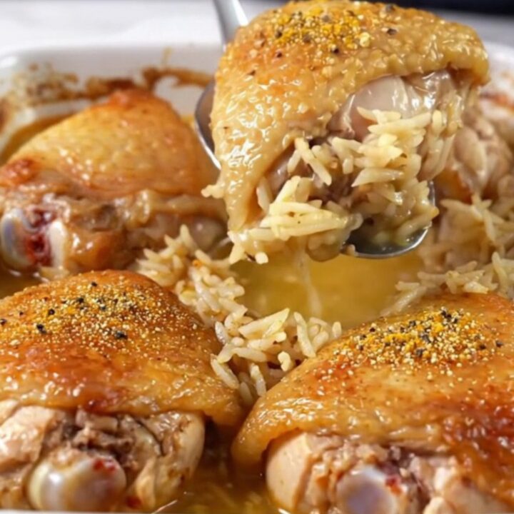 A top-down view of a rectangular baking dish filled with raw chicken thighs and rice, ready for the oven.