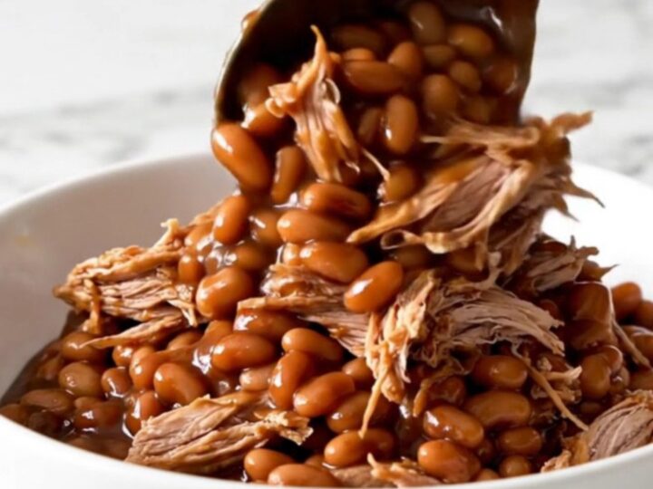 A close-up of tender shredded pork mixed with baked beans in a rich barbecue sauce.