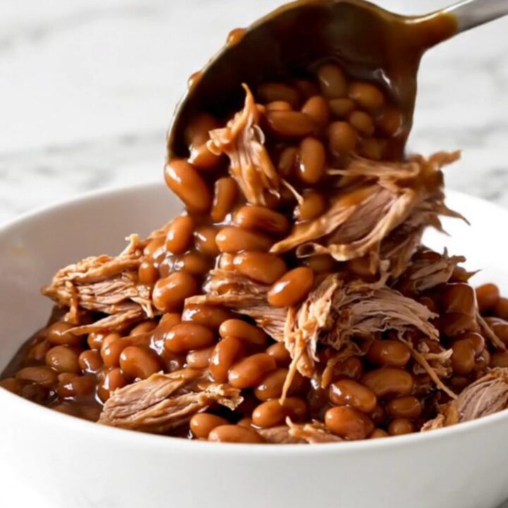 A close-up of tender shredded pork mixed with baked beans in a rich barbecue sauce.